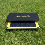 Portable SunJack solar charger on green grass, yellow frame, black panel with sun logo