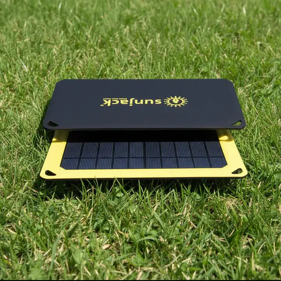 Portable SunJack solar charger on green grass, yellow frame, black panel with sun logo