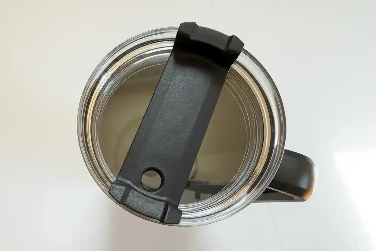 Top view of stainless steel travel mug with black lid and handle, showing interior and sip opening