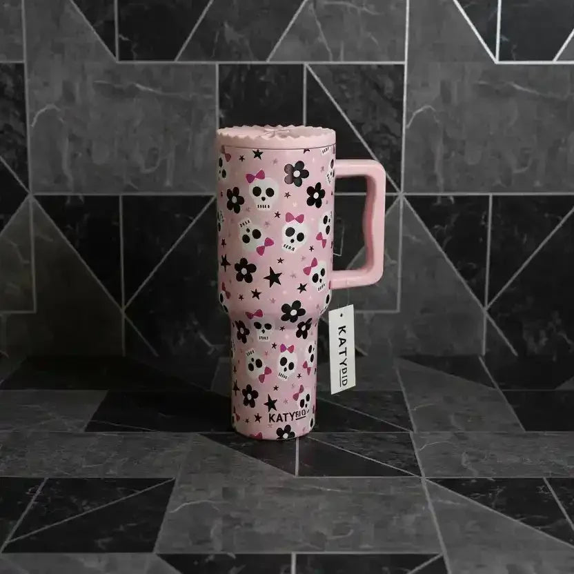 Pink travel mug with skull, flower, and star pattern, branded KATYDID, on geometric tile background