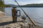 Fishing rod and lure-print travel mug on lakeside rock, natural outdoor scene
