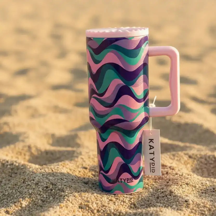Tumbler with wavy pattern and pink handle on a sandy background 