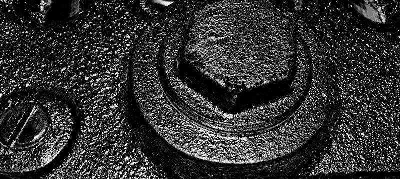 Close-up of textured metal surface with bolts, black and white industrial detail