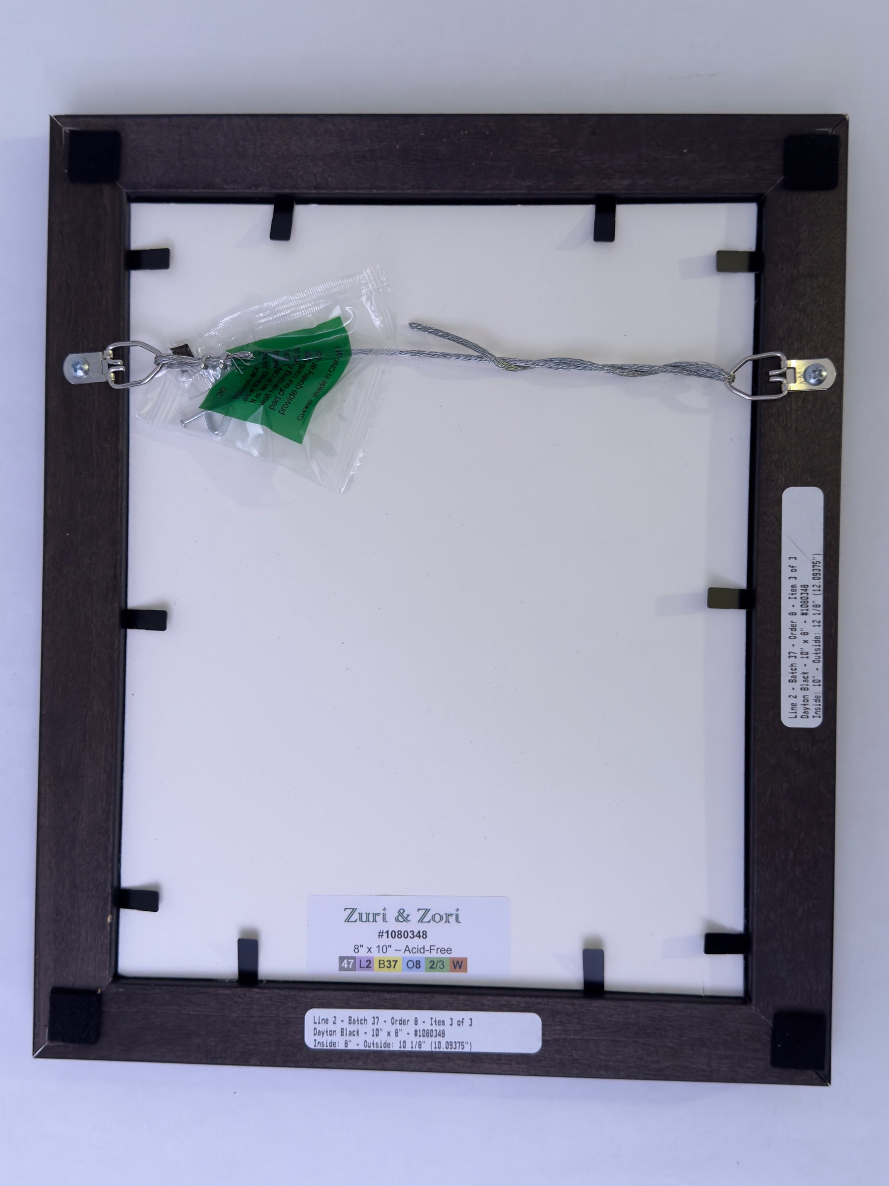 Back of a framed picture with a green leaf attached, on a white background.