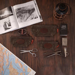 Accessory bag Collection of field tools and accessories on a wooden surface with an open book and map.