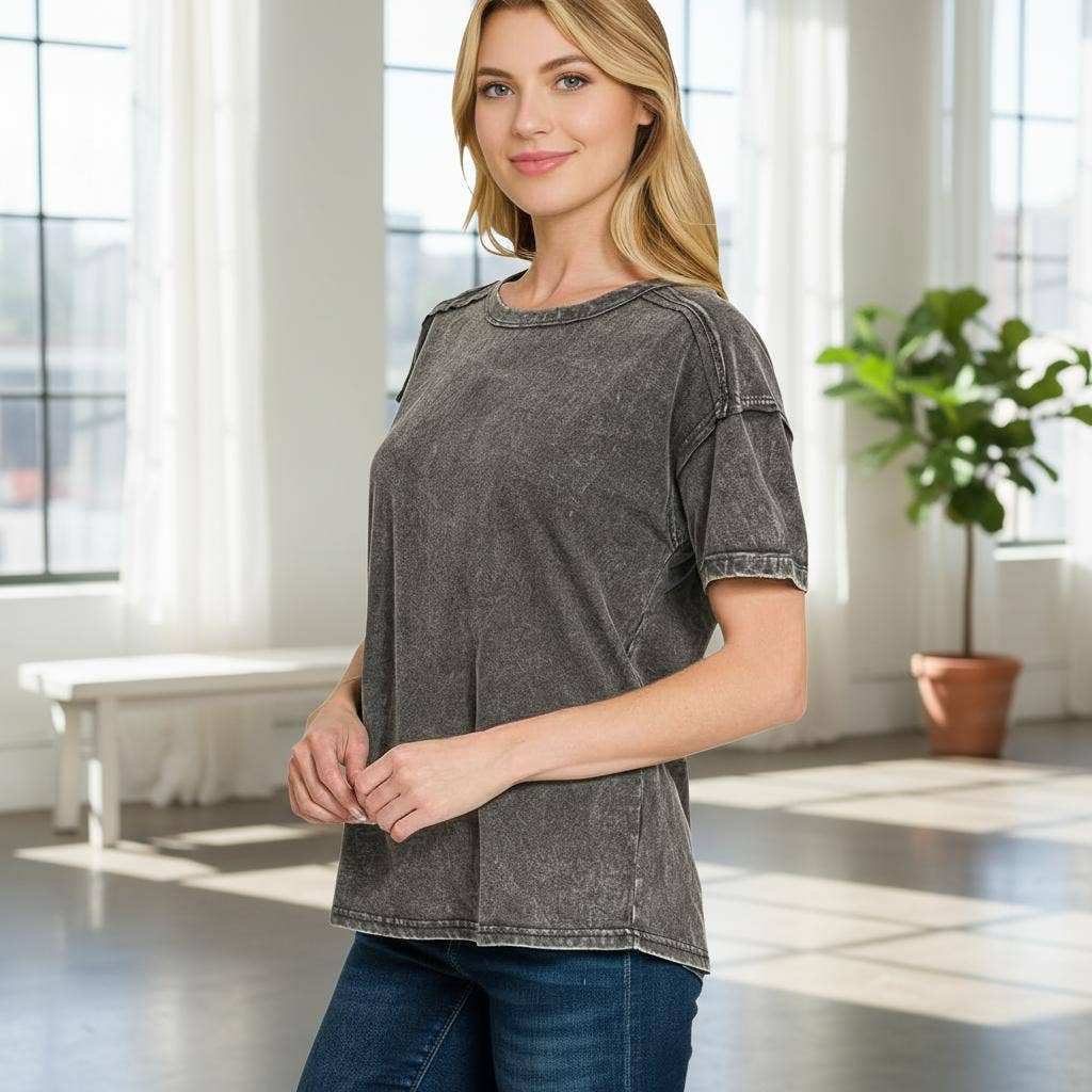 Woman wearing a gray t-shirt and blue jeans standing in a bright room with large windows.
