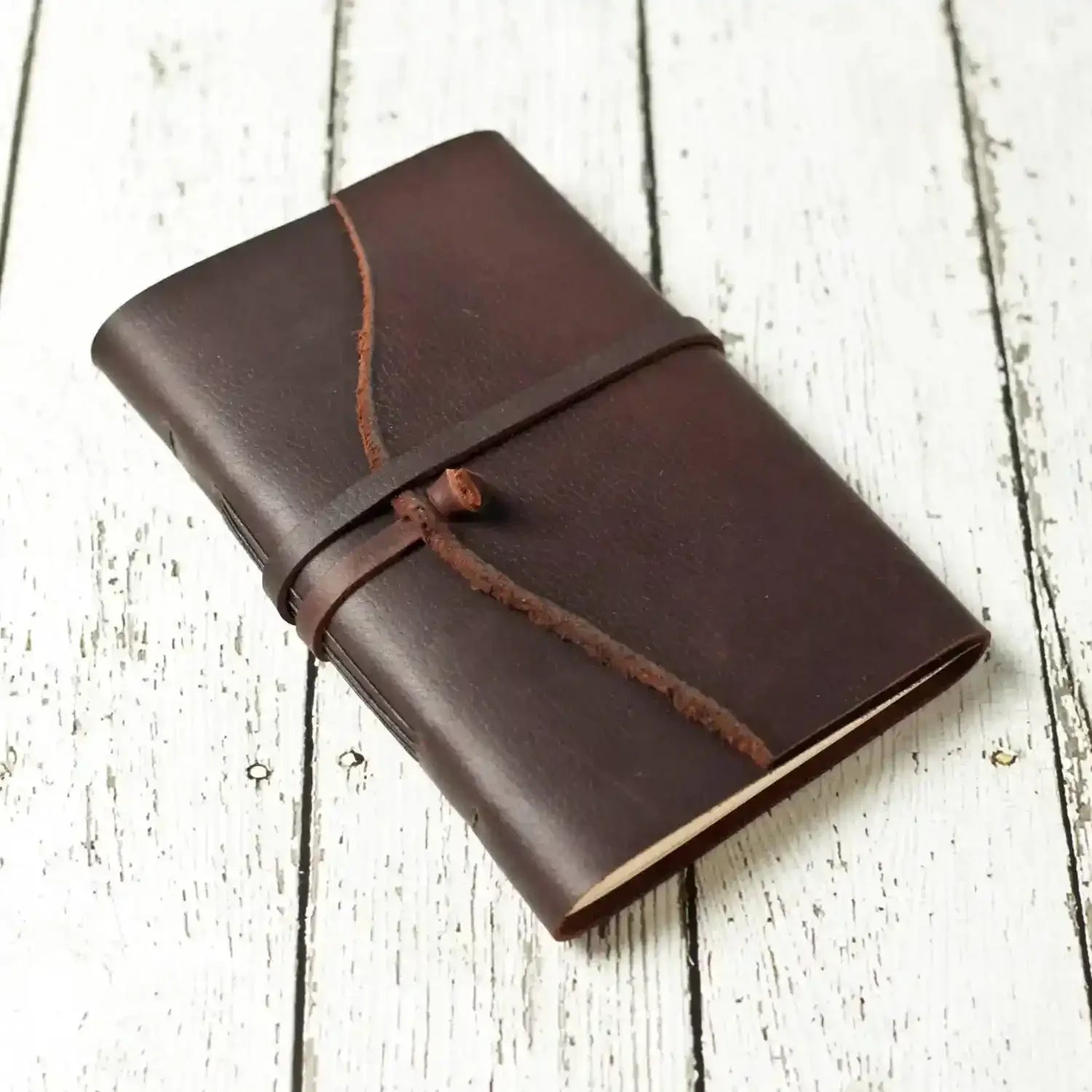 Brown leather journal with strap closure on white wood background