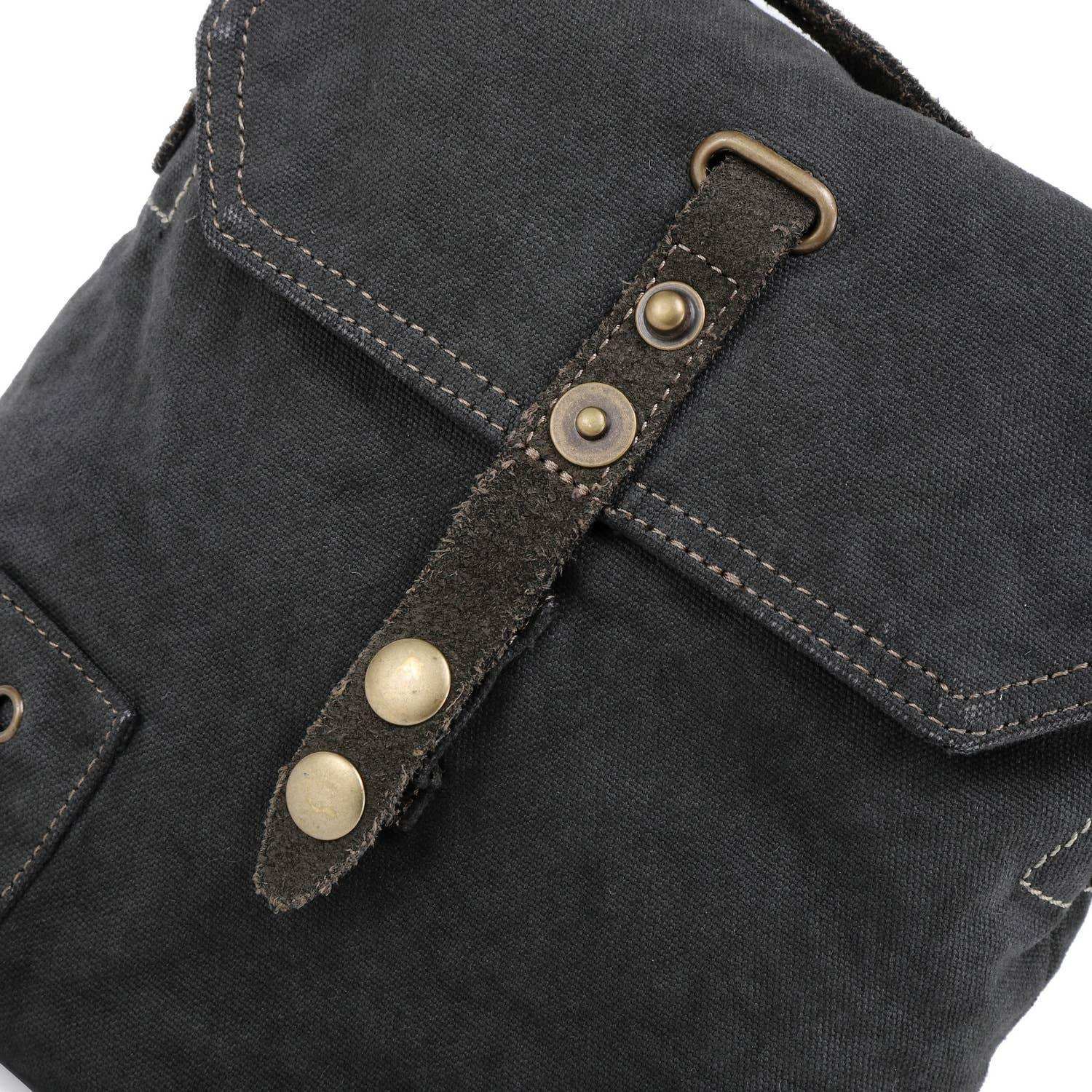 Close-up of a dark gray bag with a leather strap and brass buttons on a white background