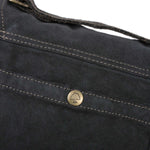 Close-up of a black bag with a gold button featuring a logo on a white background