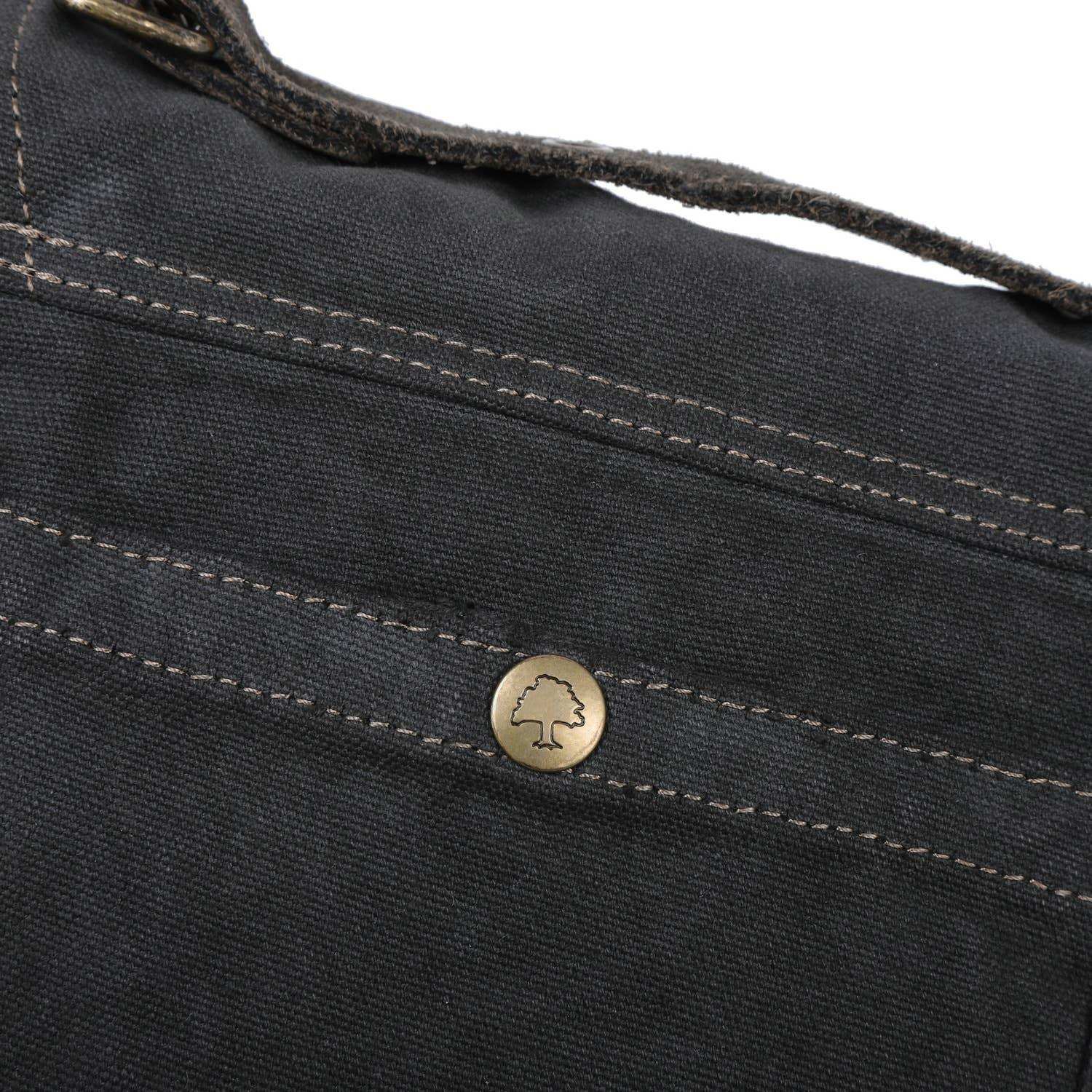 Close-up of a black bag with a gold button featuring a logo on a white background