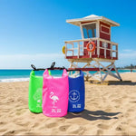 Three colorful 2L waterproof bags with turtle, flamingo, and anchor designs on sandy beach near lifeguard tower