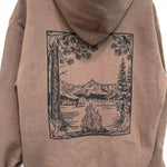 Tan hoodie with forest scene print: campfire, mountains, lake, deer, bear, raven, pine trees