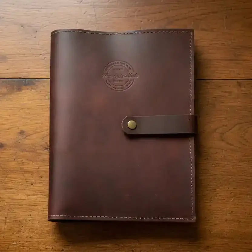 Brown leather journal with embossed logo and strap closure, resting on wooden surface