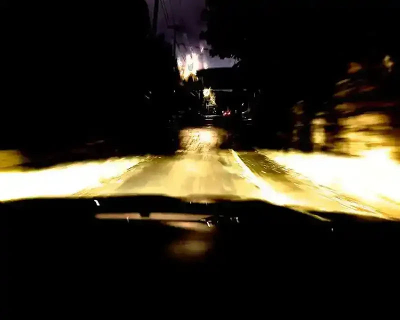Night driving view from car, headlights illuminating wet road, blurred motion, dark trees, distant lights