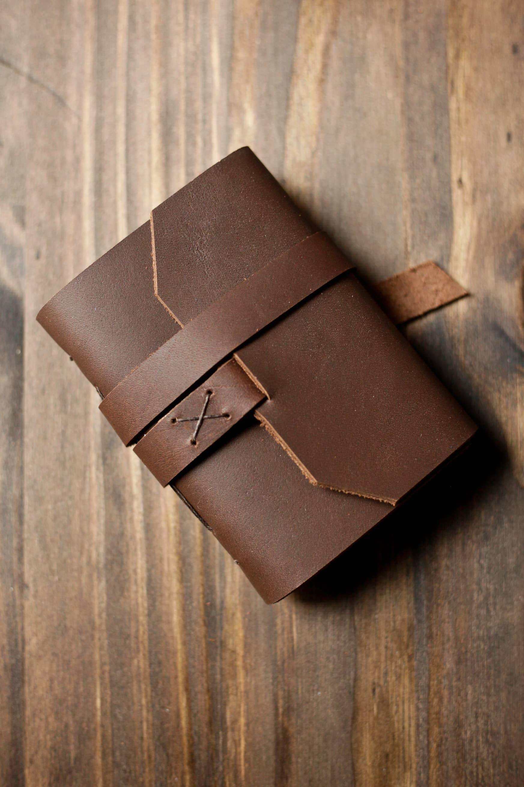 Handcrafted brown leather journal with strap closure on rustic wood surface