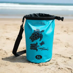 Blue 5L waterproof dry bag with sea turtle print on sandy beach, ideal for Hawaii trips and ocean adventures.