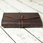 Handmade leather journal with strap closure on rustic white wood background