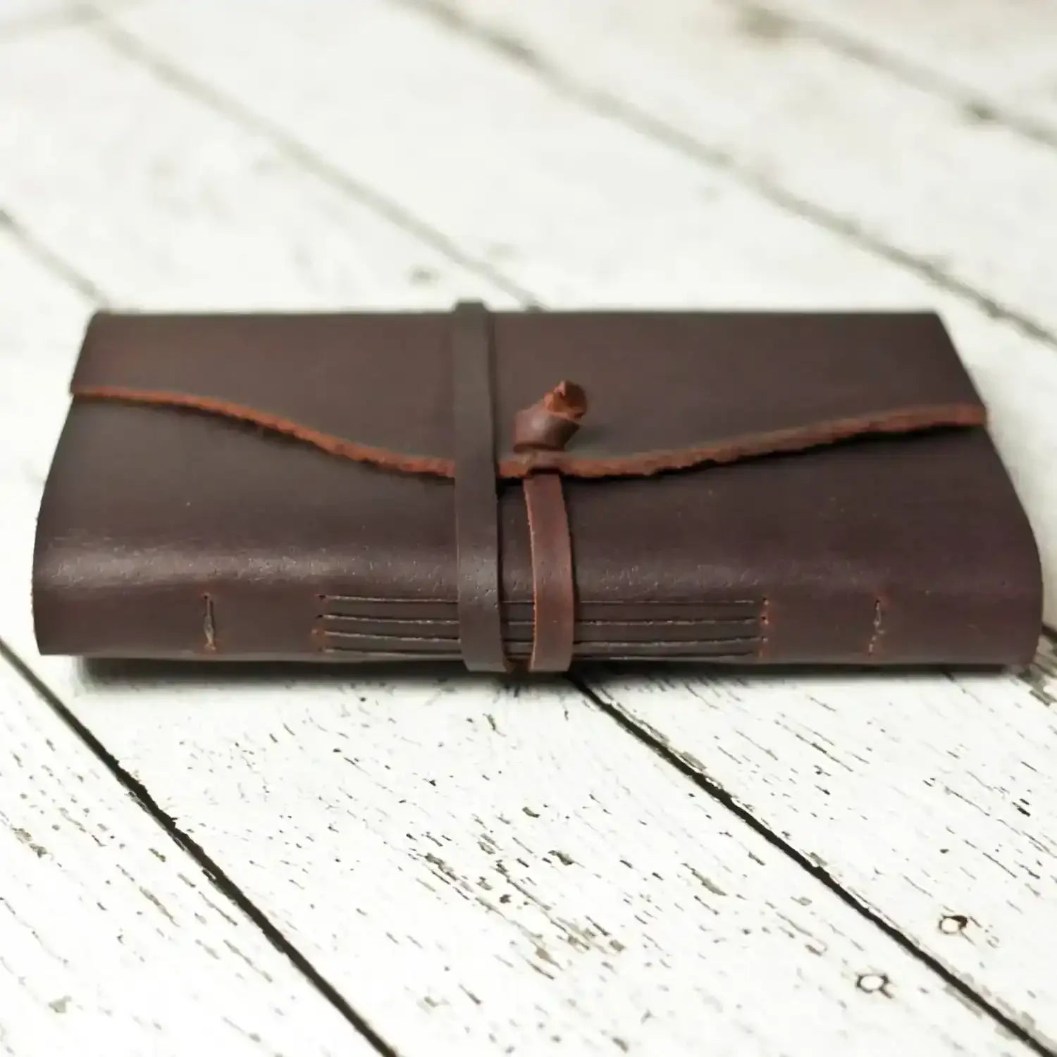 Handmade leather journal with strap closure on rustic white wood background
