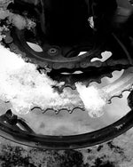 Snow-covered bicycle gear and chain in black and white, winter mechanical detail