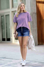 Woman wearing a purple oversized t-shirt and denim shorts standing on a street.